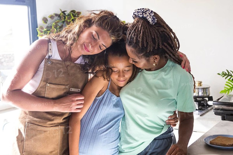 A heartfelt moment shared between two women and their daughter in a kitchen, symbolizing love, unity, and acceptance within a lesbian family, highlighting LGBTQIA+ pride