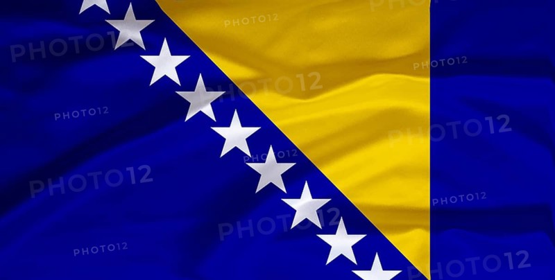 National flag of Bosnia and Herzegovina, in front of cumulus clouds and blue sky, studio
