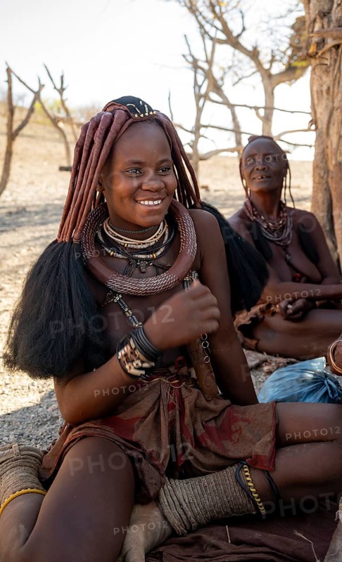 Traditionally dressed young Himba woman sitting in the shade, near Opuwo, Kaokoveld, Kunene, Namibia