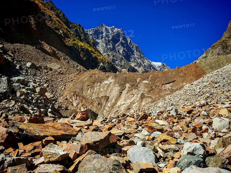Glacier edge, rugged scree field leading to high mountains under a clear blue sky, hiking to Chalaadi Glacier, Mestia, Svaneti, Georgia