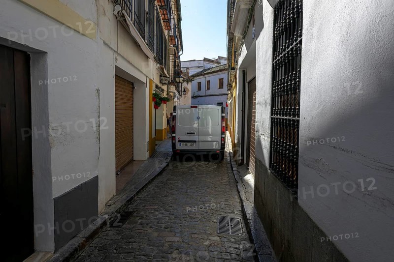 Narrow paved street with parked van between tall, shady walls, Cordoba, Spain