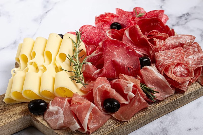 Assorted meat, appetizer, prosciutto, salami and ham, with maasdam cheese and olives, on a wooden board, breakfast, top view, close-up, no people