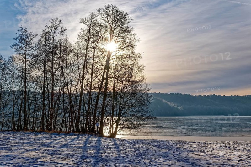 There is snow on the shore and the sun shines through the bare winter trees on Lake Werbellin in the UNESCO Schorfheide-Chorin Biosphere Reserve. Joachimsthal, Schorfheide, Brandenburg, Germany