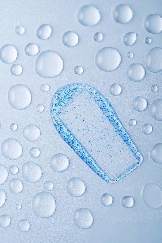 Close-up of a face scrub smear with blue micro-exfoliating particles on a light surface, surrounded by water droplets Perfect for promoting skincare and beauty products