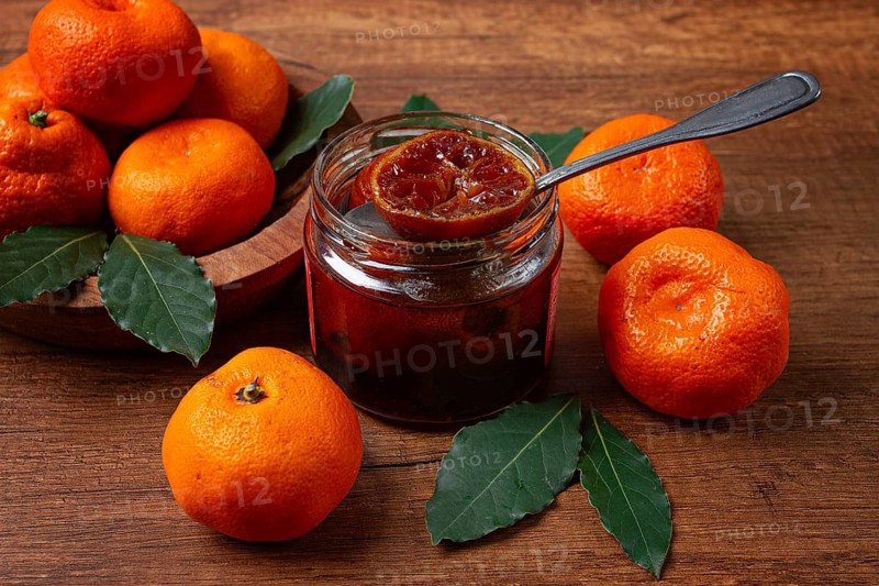 Jar of tangerine jam, stands on a wooden table, with fresh tangerines