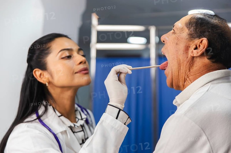 A female doctor performs a routine medical examination on an elderly male patient, assessing his throat with professional care and precision in a clinical setting