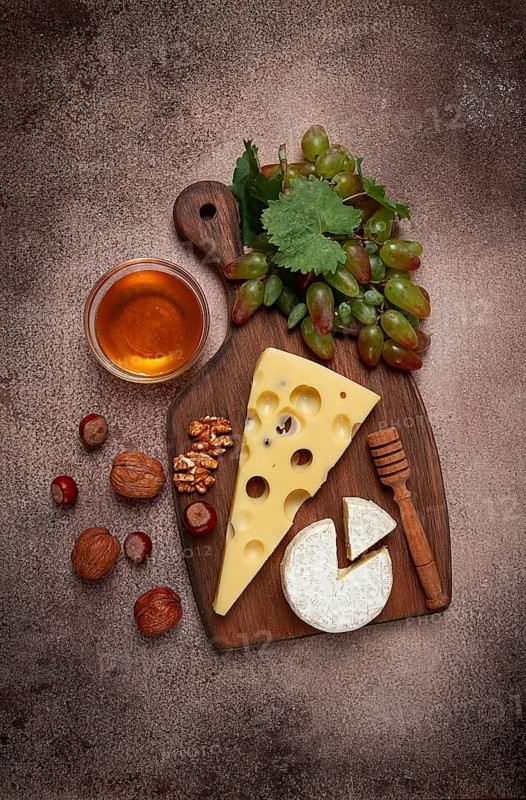 Cheese with big holes, emmental, maasdam, brie cheese, on a cutting board, with grapes and honey, nuts, appetizer to wine, top view