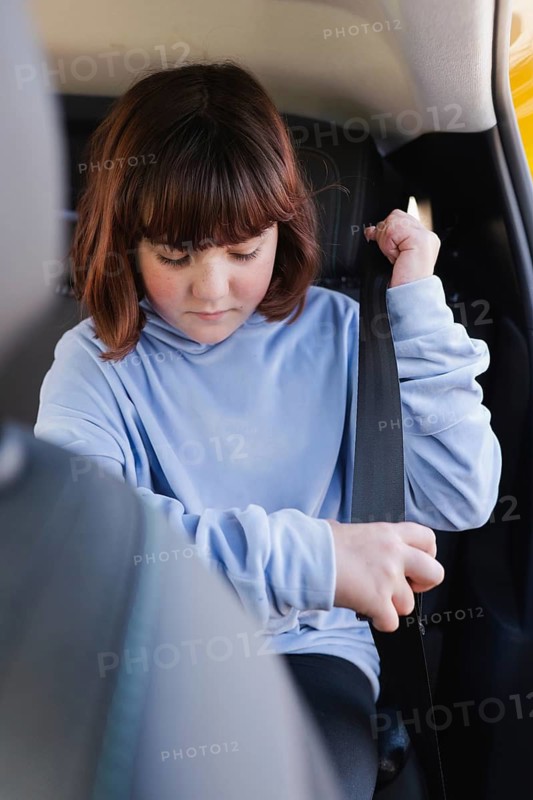 A child in a light blue hoodie fastens the seatbelt in the backseat of an electric car. Focus on safety and comfort in a modern vehicle setting
