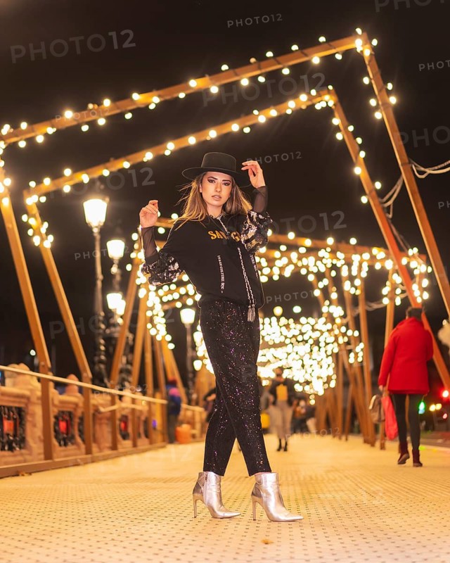 Christmas lights in the city, Caucasian blonde girl dressed in black and with sequins walking on an illuminated bridge, winter lifestyle