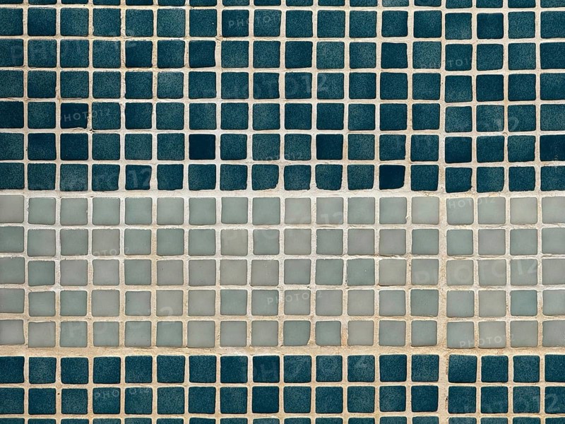 A close-up view of a wall featuring a pattern of square tiles. The arrangement includes alternating rows of dark blue and light beige squares, creating a striking geometric design