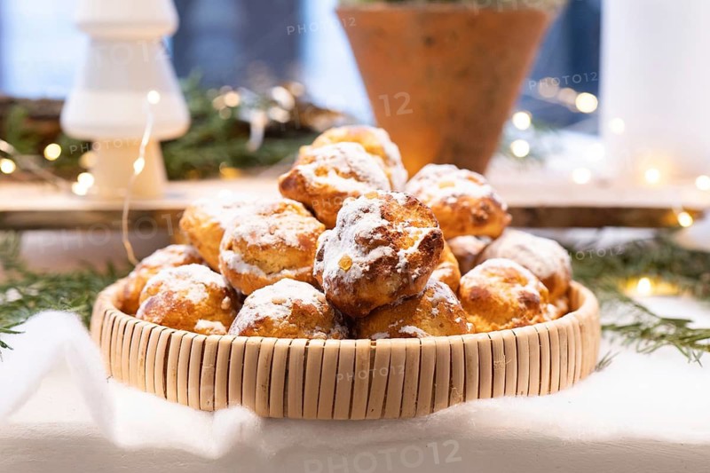 A basket filled with delicious pastries dusted with powdered sugar, set on a festive holiday table. The background is adorned with soft lights and greenery, creating a cozy atmosphere