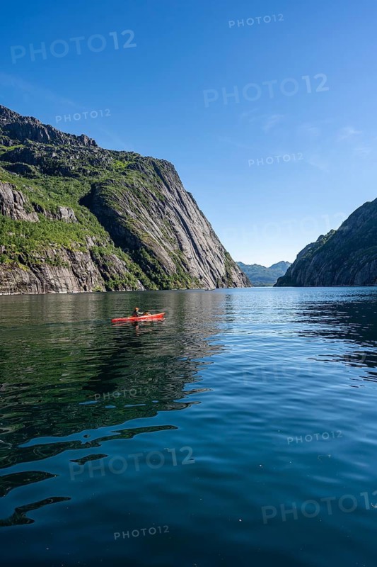 Kayaker with red kayak in the fjord Trollfjord, mountain peaks reflected in the water, fjord landscape and mountains, Lofoten, Nordland, Norway