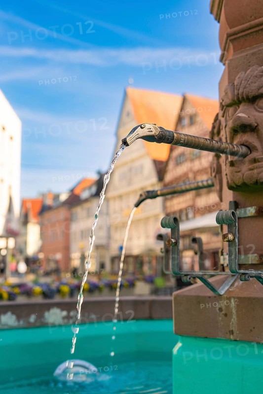 Close-up of flowing water from a fountain spout with historic buildings, Nagold, Black Forest, Germany