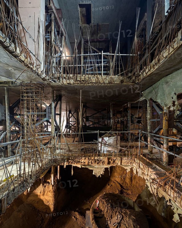 View of an underground construction site with layers of concrete and exposed reinforcing bars. The scene captures the complex network of scaffolding during excavation