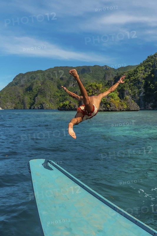 Tourist diving from a traditional bangka boat into the clear turquoise water of the twin lagoon on coron island, philippines