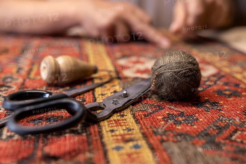 Cropped unrecognizable senior male Iranian carpet restorer meticulously works on repairing a patterned rug with tools in Salzburg, Austria
