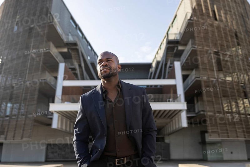 A business cuban man in a suit stands confidently outside a modern office building, exuding professionalism and leadership. The backdrop features contemporary architecture
