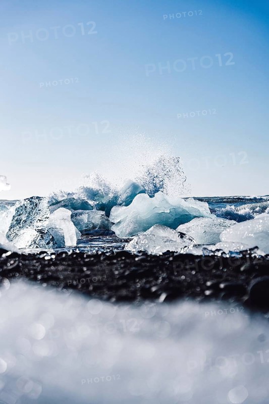 Captivating ice formations on Diamond Beach, Iceland, contrast against the black sand, with waves crashing dynamically in the background under a clear blue sky