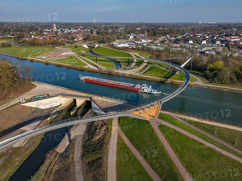 Castrop-Rauxel, North Rhine-Westphalia, Ruhr region, Germany - Sprung bridge over the Emscher, here with barge on the Rhine-Herne Canal, a footbridge and cycle bridge across the Emscher and the Rhine-Herne Canal. EMSCHERLAND adventure park, new nature and water adventure park on the restored Emscher, at the Emscher water cross with the Rhine-Herne Canal on the city limits of Recklinghausen and Castrop-Rauxel. Flood protection through area expansion. The ecological focus at the confluence of the Suderwicher Bach and Emscher rivers will also be a future garden of the IGA 2027 International Garden Exhibition. Before the restoration, the river system of the Emscher was an open, aboveground waste water channel, mixed water channel with surface water and waste water