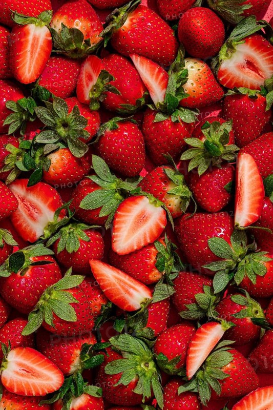 From above, a vibrant array of fresh strawberries showcases their rich red hues with green leaves, offering a tempting and colorful visual perfect for summer themes