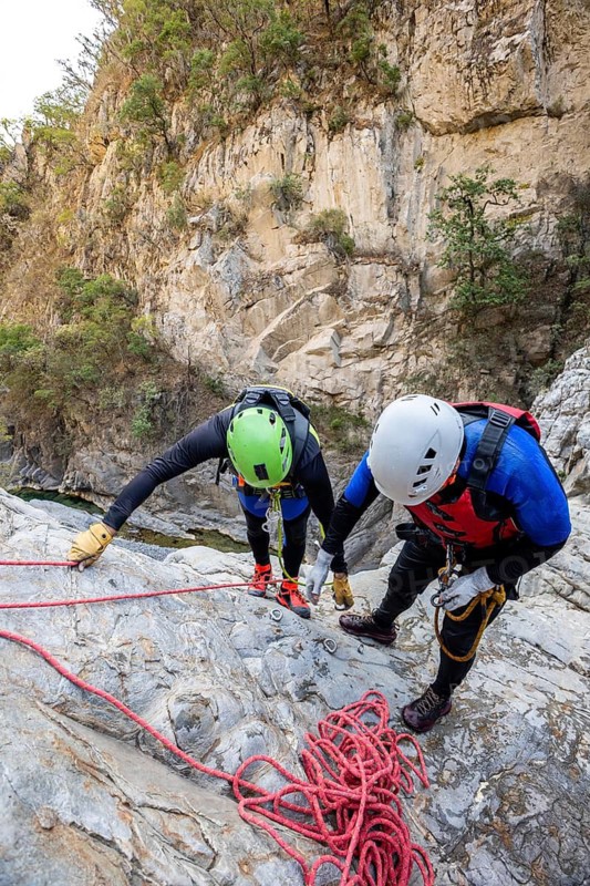 Two canyoneers equipped with safety gear meticulously prepare for a thrilling descent in the rugged landscape of Matacanes, Nuevo Leon, Mexico, epitomizing adventure and teamwork