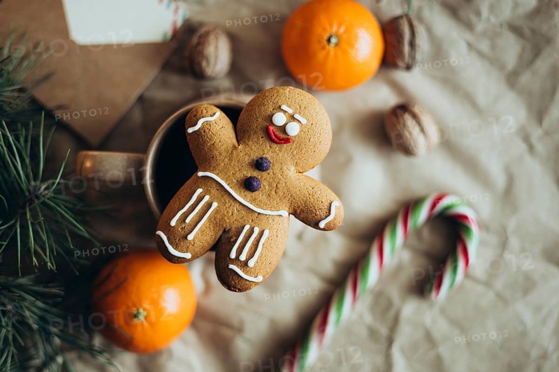 A charming gingerbread man cookie is surrounded by festive elements like oranges, walnuts, candy cane, and pine branches, creating a cozy holiday atmosphere