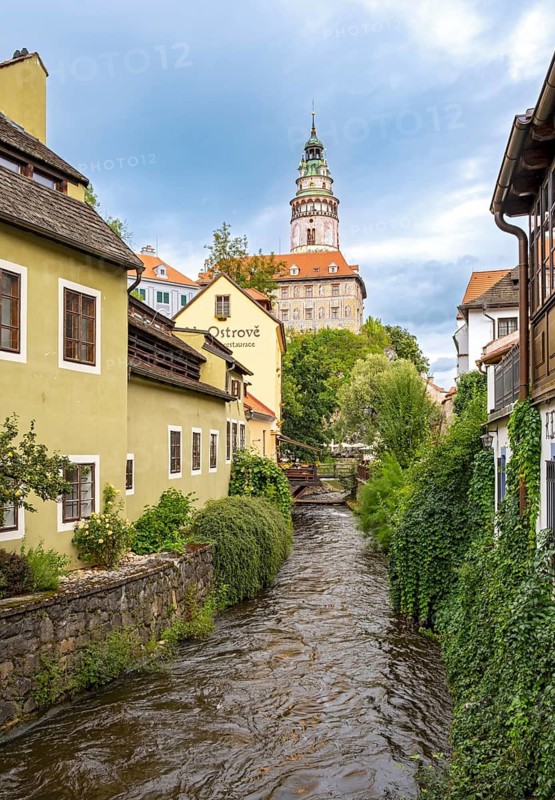 View of Ceský Krumlov Castle tower from a street with buildings and a stream, Cesky Krumlov, Czech Republic