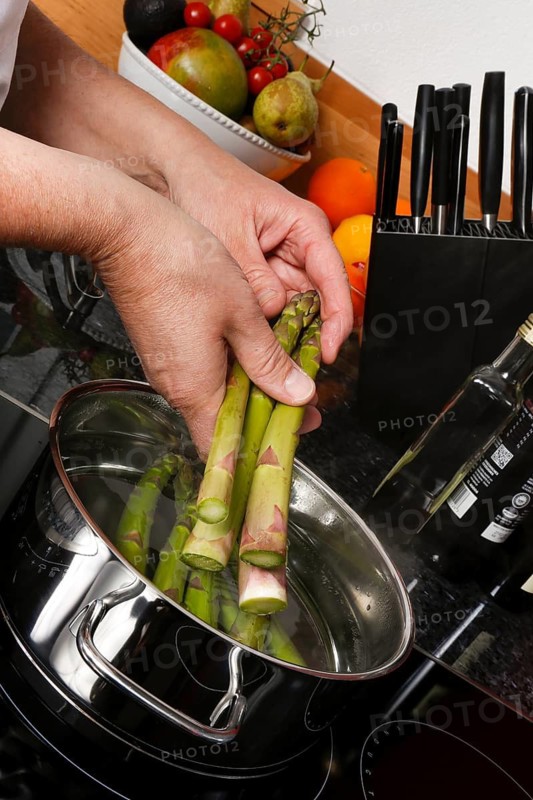 South German cuisine, vegetables, vegetarian, preparation of green asparagus with rhubarb vinaigrette and potato gratin, add raw asparagus to cooking water, saucepan, cooking sheet, induction cooker, ceramic hob, healthy, traditional cuisine reinterpreted, men's hands, food photography, studio, Germany