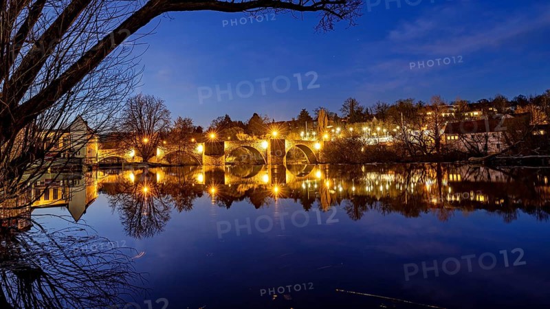 Evening scene with illuminated bridge and reflecting river at night, The historic Bartenwetz stone bridge of Melsungen
