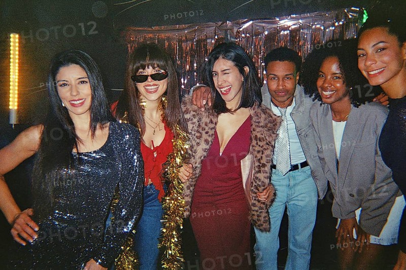 Diverse group of friends posing and smiling at a vibrant retro themed night party, enjoying glittery fashion, analog film vibe and warm, nostalgic nightlife energy