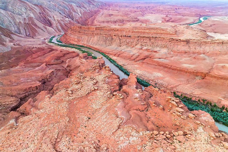 Stunning aerial shot of the Rio San Juan curving through the deeply eroded, colorful red rock landscapes of Utah. The river's vibrant green waters contrast starkly against the arid, layered terrain