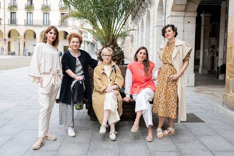 A group of five stylish women pose confidently on a city street. They exhibit unique fashion styles, embodying creativity and empowerment in a vibrant public setting