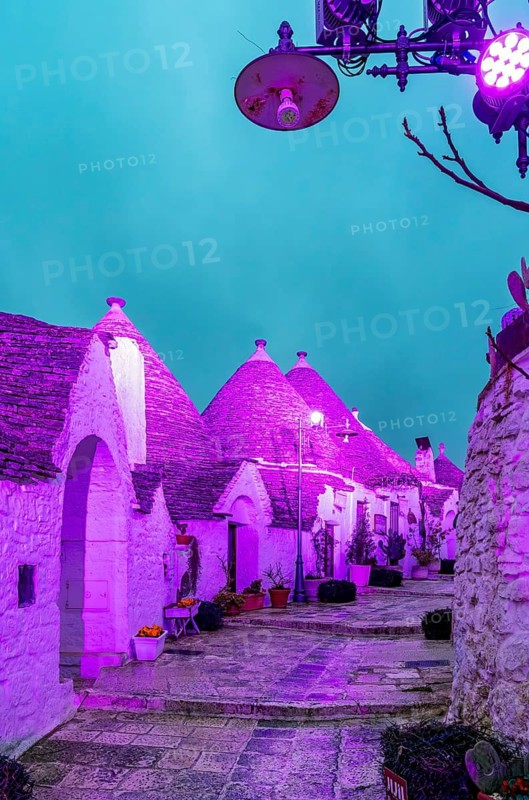 Trulli houses illuminated in purple light, Rione Monti, Alberobello, Apulia - Puglia, Italy