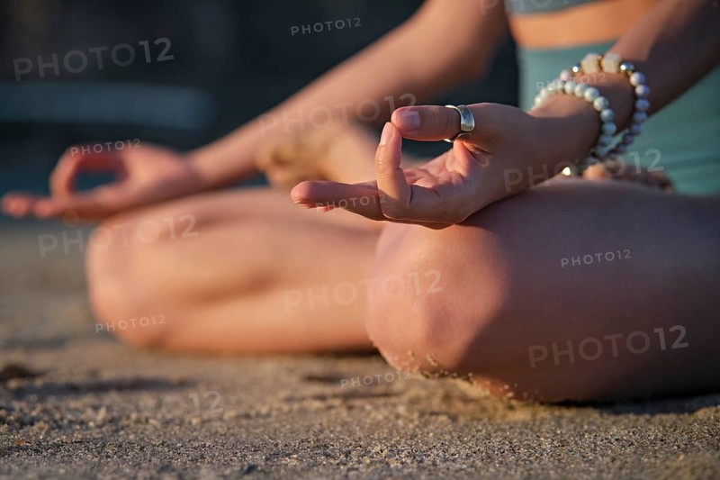 Woman meditates in Padmasana on the beach, performing Chin mudra hand gesture during a peaceful yoga practice at sunset