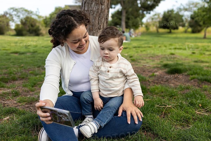 A mother and her baby share a joyful moment in the park. They sit together on the grass, surrounded by nature, capturing memories that will last a lifetime