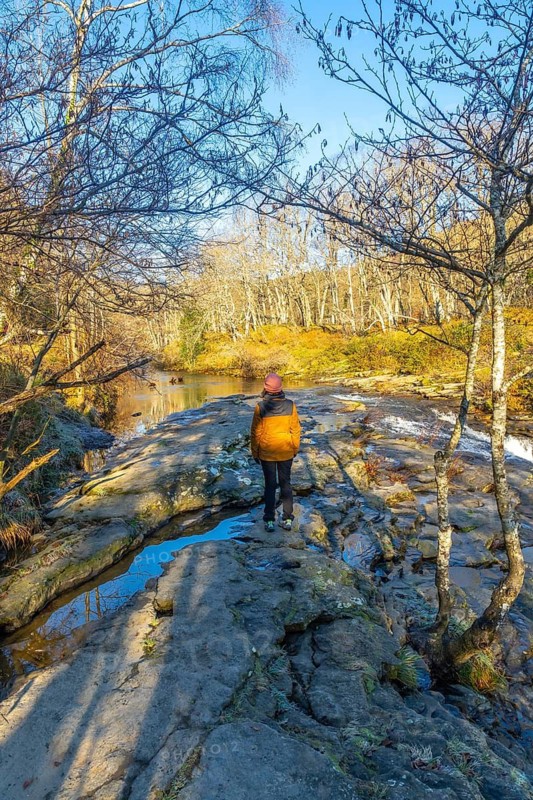 Hiker standing on rocks admiring the baias river in zaldibartxo pool, gorbeia natural park, basque country, on a sunny winter day