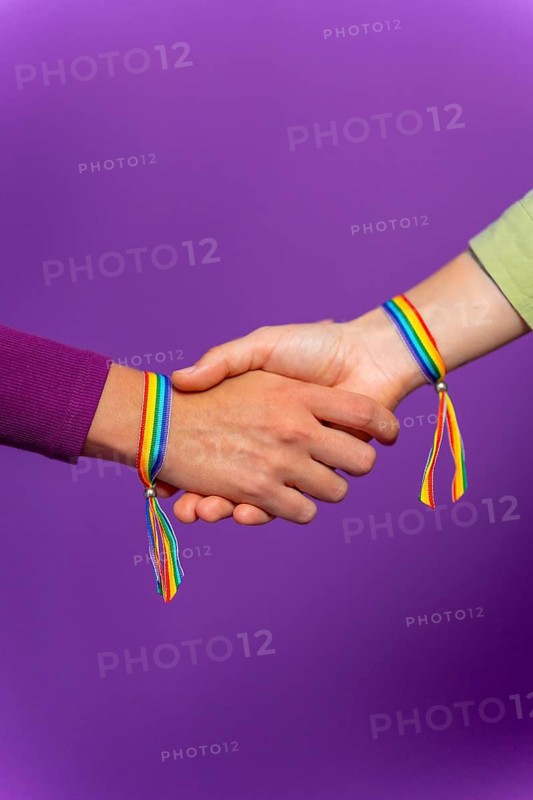 Vertical studio photo with purple background of the hands of unrecognizable lesbian female couple with LGBT rainbow bracelet