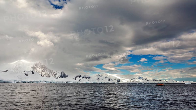 Snowy mountain landscape by the sea under a dramatic sky with dark clouds and a small boat, The landscape of Antarctica