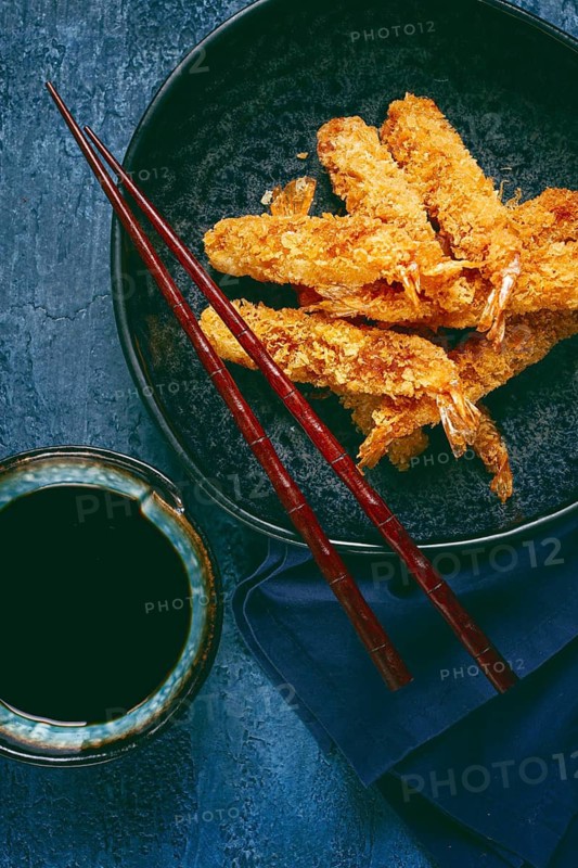 Shrimp in tempura, deep fried, on a black plate, with soy sauce, close-up, top view, no people