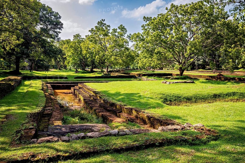 Historic ruins in a green landscape with trees under a clear, sunny sky, The Lion Gate at Lion's Rock near Sigiriya in Sri Lanka