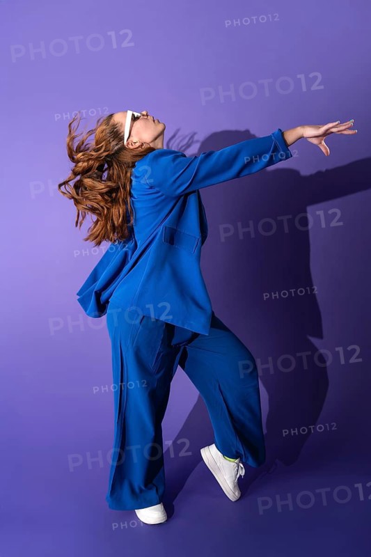A young woman dancer in a vibrant blue outfit gracefully performs against a striking purple background. Her movement and expression capture the essence of modern dance