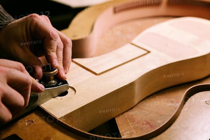 Hands meticulously crafting a bass guitar body in a luthier‚Äôs workshop. The image captures the precision and care involved in shaping wood into a musical instrument