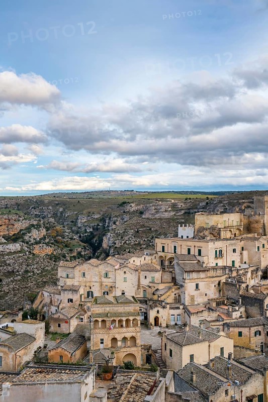 Captivating view of Matera's historic stone buildings blending with the rugged surrounding landscape, showcasing timeless architecture and natural beauty under a cloudy sky