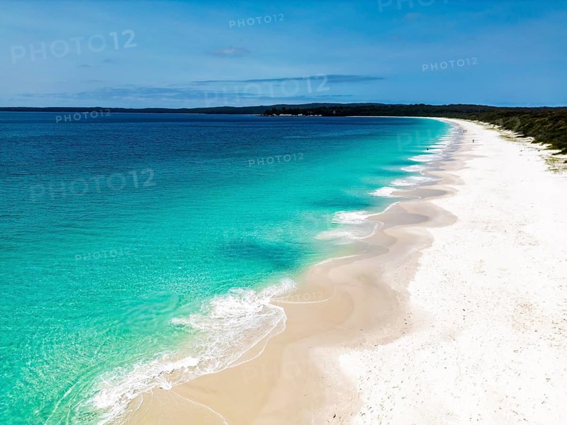 A picturesque view of a tranquil beach with clear turquoise water meeting a pristine white sandy shoreline in Jervis Bay, perfect for relaxation and a tropical escape