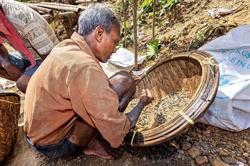 A man carefully squats and sorts stones in a large basket, the sapphire and gemstone mines at Ratnapura in Sri Lanka