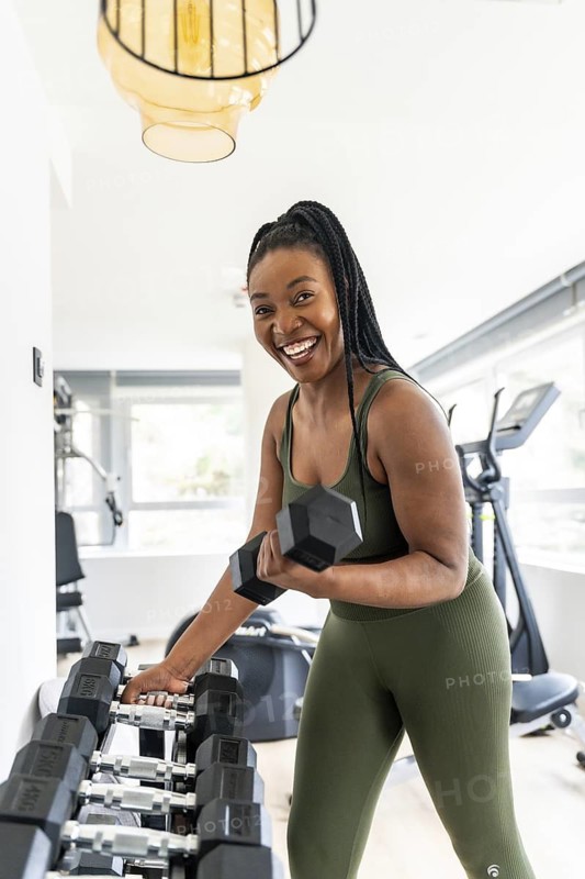 Smiling businesswoman picks up a dumbbell while exercising in a hotel gym during her business trip, promoting health and fitness on the go