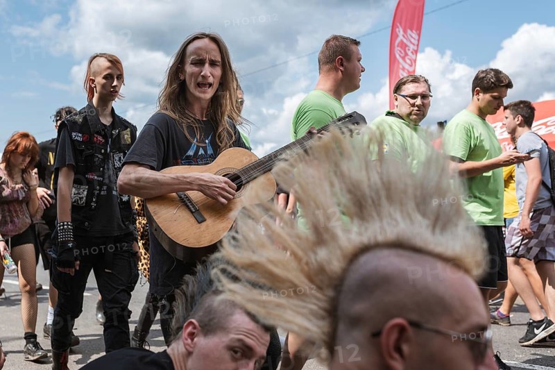 KOSTRZYN NAD ODRA, POLAND - AUGUST 1, 2019: Singing man with guitar passing near men with Iroquois hair during music festival Pol'and'Rock.