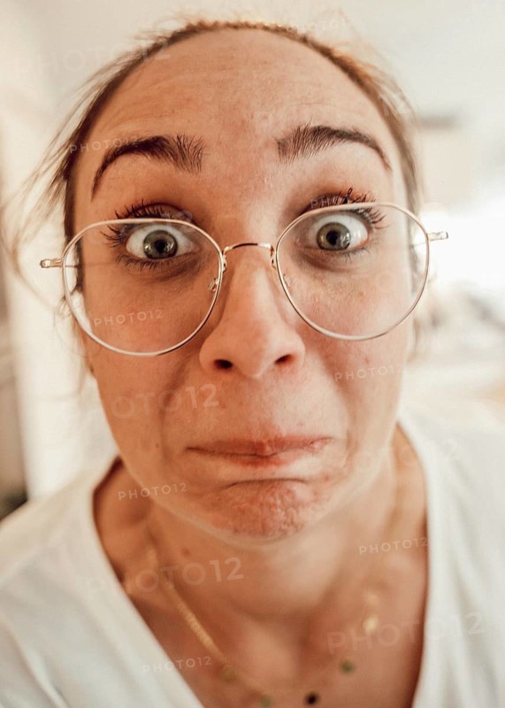 A woman with large glasses looks into the camera in surprise