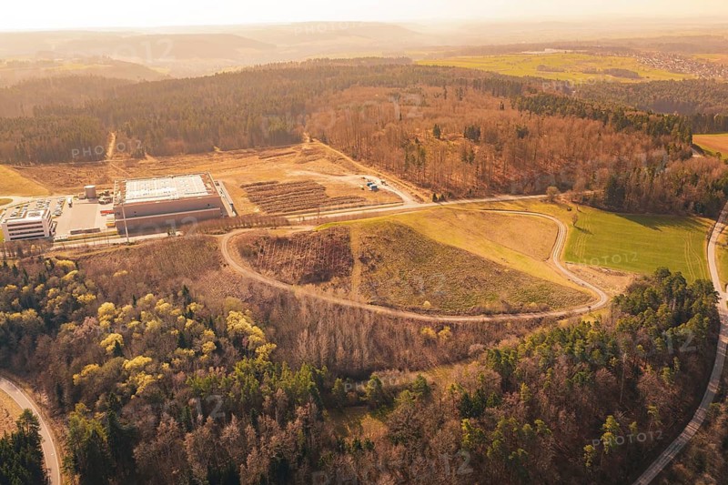 Wide view of a hilly area with industrial buildings, surrounded by forest and fields, old deposit in front of PV Bau, Lindenrain, Calw, Germany