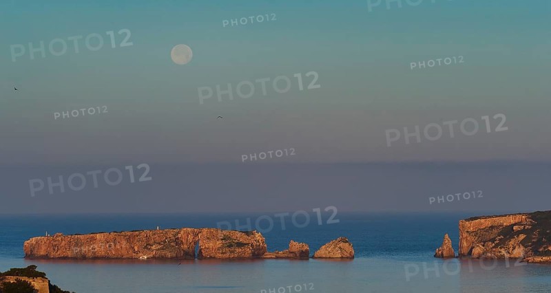 A full moon over rocks in the sea with a clear sky and some birds, morning light, Tsichli Baba island, Sfaktiria island, Navarino Bay, Pylos, Peloponnese, Greece